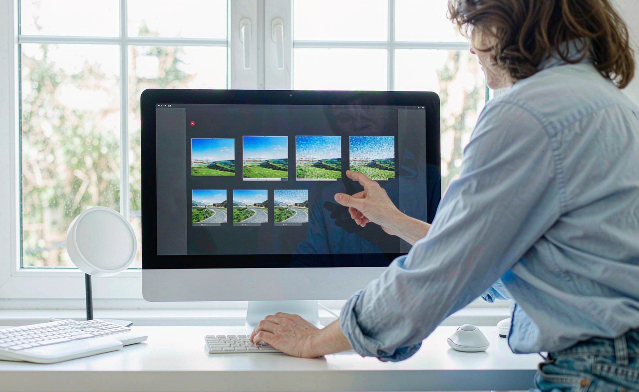 A person comparing photo thumbnails on a large desktop monitor in a bright home office