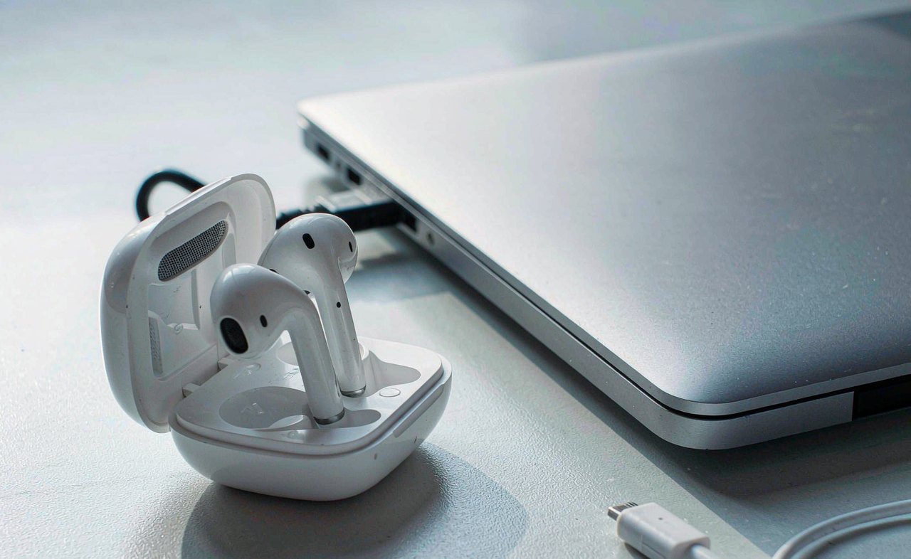 White wireless earbuds in an open charging case resting beside an open laptop on a clean desk