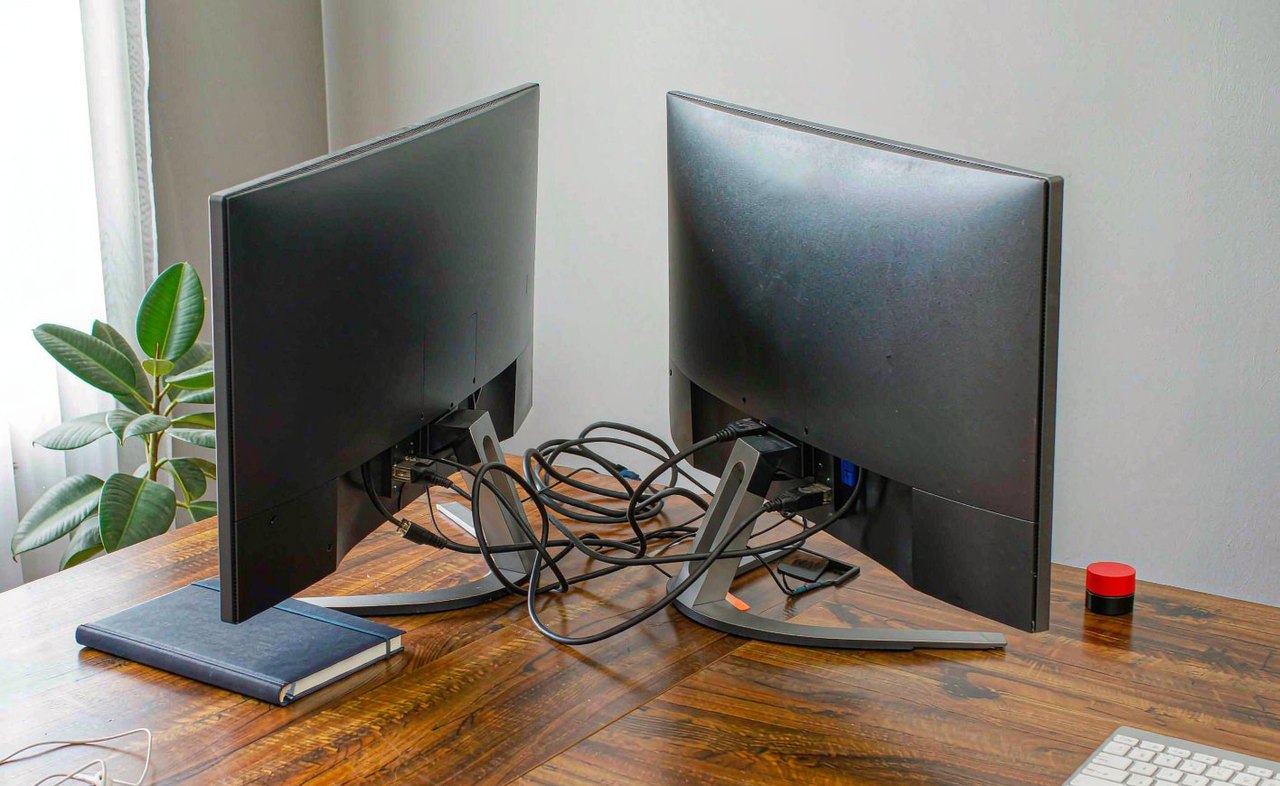 A dual-monitor workstation on a walnut desk with visible cables behind the two screens